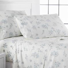 a bed with white sheets and blue flowers on the comforter, next to a night stand