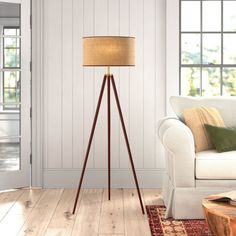 a living room with a white couch and wooden floor lamp next to a large window