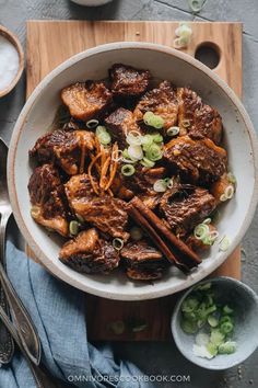 a bowl filled with meat and vegetables on top of a wooden cutting board next to spoons