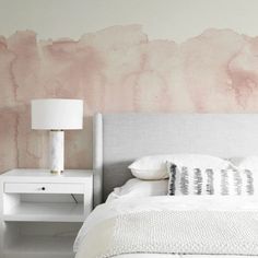 a white bed sitting next to a pink wall with watercolor stains on the walls