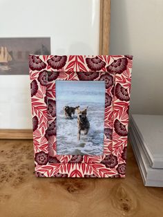 a red and white photo frame with a dog in the water on top of a wooden table