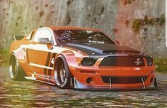 an orange and black car parked in front of a stone wall