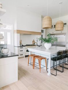 a large kitchen with white cabinets and wooden floors is pictured in this image, there are four stools at the center of the island