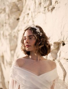 a woman in a white dress standing next to a rock wall wearing a flower crown