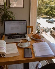 an open book sitting on top of a wooden table next to a laptop computer and cup of coffee