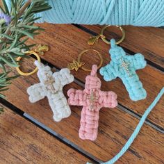 three crocheted cross key chains sitting on top of a wooden table next to a ball of yarn