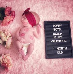 a baby laying on top of a pink blanket next to flowers and a sign that says sorry, daddy is my valentine 1 month old