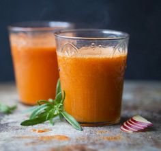 two glasses filled with orange juice sitting on top of a stone table next to an onion slice