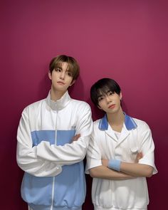 two young men standing next to each other in front of a purple wall with their arms crossed