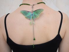 a woman's back with a butterfly tattoo on her shoulder and green beads hanging from it