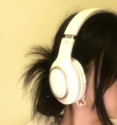 a woman with black hair wearing white headphones on her ear and looking at the wall