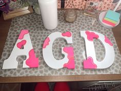 the letters are decorated with pink and white paint on top of a wooden table next to a candle