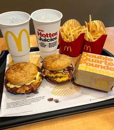 two hamburgers and fries on a tray with paper cups next to them at a mcdonald's restaurant