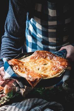 a person holding a large pot pie in their hands, with other food on the table