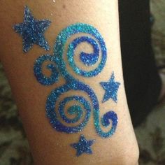 a woman's leg with blue glitter tattoos and stars on the side of it