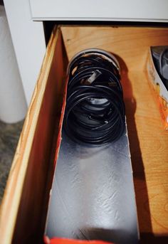 an open drawer with some black cords and other items on the bottom shelf next to it