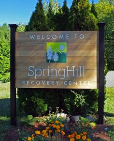 the welcome sign to springhill recovery center in front of some trees and bushes with orange flowers