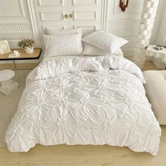 a bed with white comforter and pillows in a room next to a table on the floor