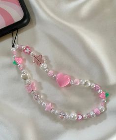 a pink and white beaded necklace with hearts on it next to a cell phone