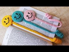 three crocheted bookmarks with faces on them sitting next to an open book