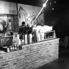 a black and white photo of a brick counter with coffee cups on it in front of a mural