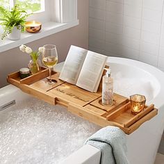 an open book and two glasses on a tray in a bathtub next to a window