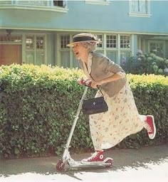 an older woman is riding her scooter down the street in front of a house