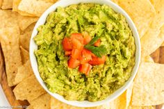 a white bowl filled with guacamole surrounded by tortilla chips and tomatoes