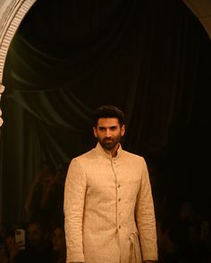 a man standing in front of a mirror wearing a white suit and tie with his hands on his hips