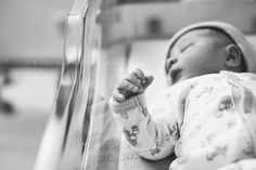 a black and white photo of a baby in a crib with his hand up to the side