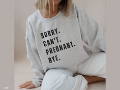 a woman sitting on the ground wearing a sweatshirt that says sorry can't pregnant bye