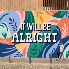 a woman walking past a colorful wall with the words it will be alright