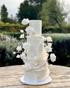 a three tiered white wedding cake with flowers on the top and bottom, sitting on a wooden table