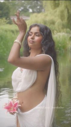 a woman in a white sari is holding her hand up to the side while standing in water