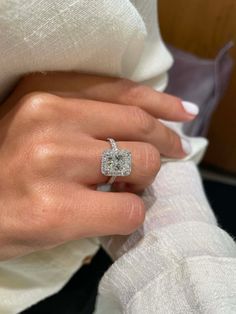 a woman's hand with a diamond ring on top of her left hand, wearing a white shirt