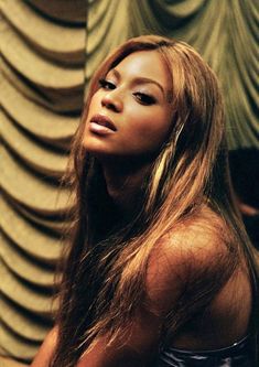 a woman with long hair standing in front of a wall and looking off into the distance