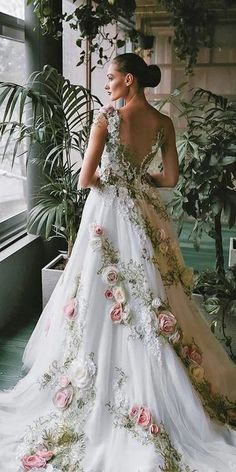 a woman wearing a wedding dress with flowers on it standing in front of a window