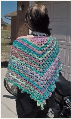 a woman standing next to a motorcycle wearing a colorful crocheted shawl