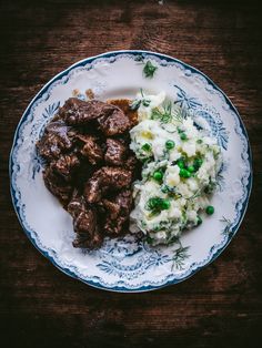 a white plate topped with meat and mashed potatoes on top of a wooden table