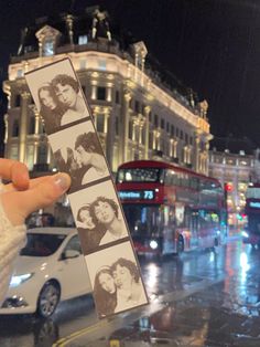 a person holding up two photos in front of a double decker bus on a city street