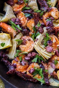 a pan filled with pasta and shrimp next to lemon wedges