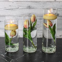 three glass vases with flowers and candles in them