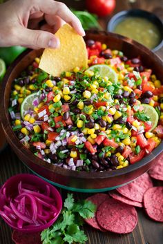 a person dipping a tortilla into a bowl filled with black beans and corn