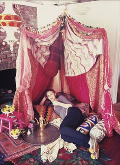 a woman laying on top of a bed covered in pink and white draping