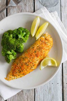 a white plate topped with fish, broccoli and lemon wedges on top of a wooden table