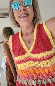 an older woman wearing sunglasses and a knitted top is smiling at the camera with her arms behind her back