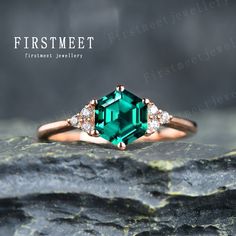 an emerald colored ring with three diamonds on it's sides, sitting on top of a rock