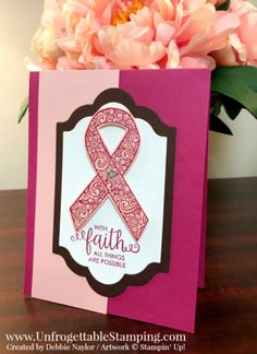 a card with a pink ribbon on it and some flowers in the vase behind it