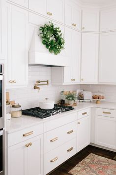 a kitchen with white cabinets and gold handles on the stove top, along with a potted plant