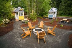 there are many chairs around a fire pit in the yard with two tiny houses behind it